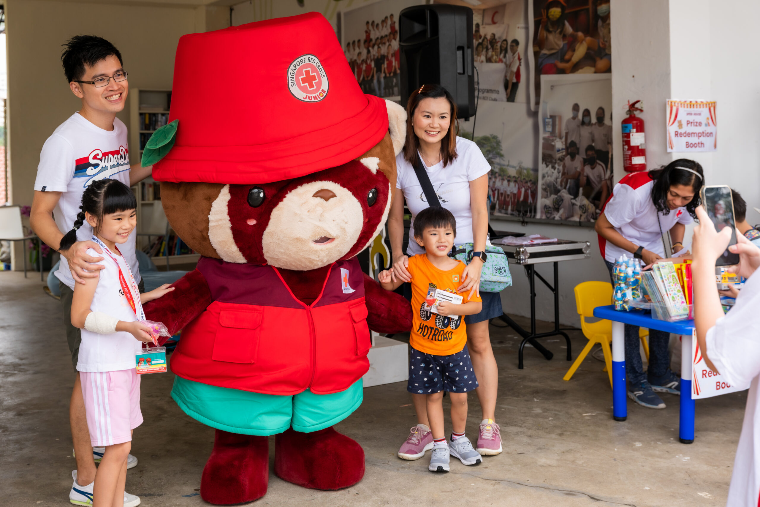 Red Cross Junior mascot posing with a family at RCJ Open House