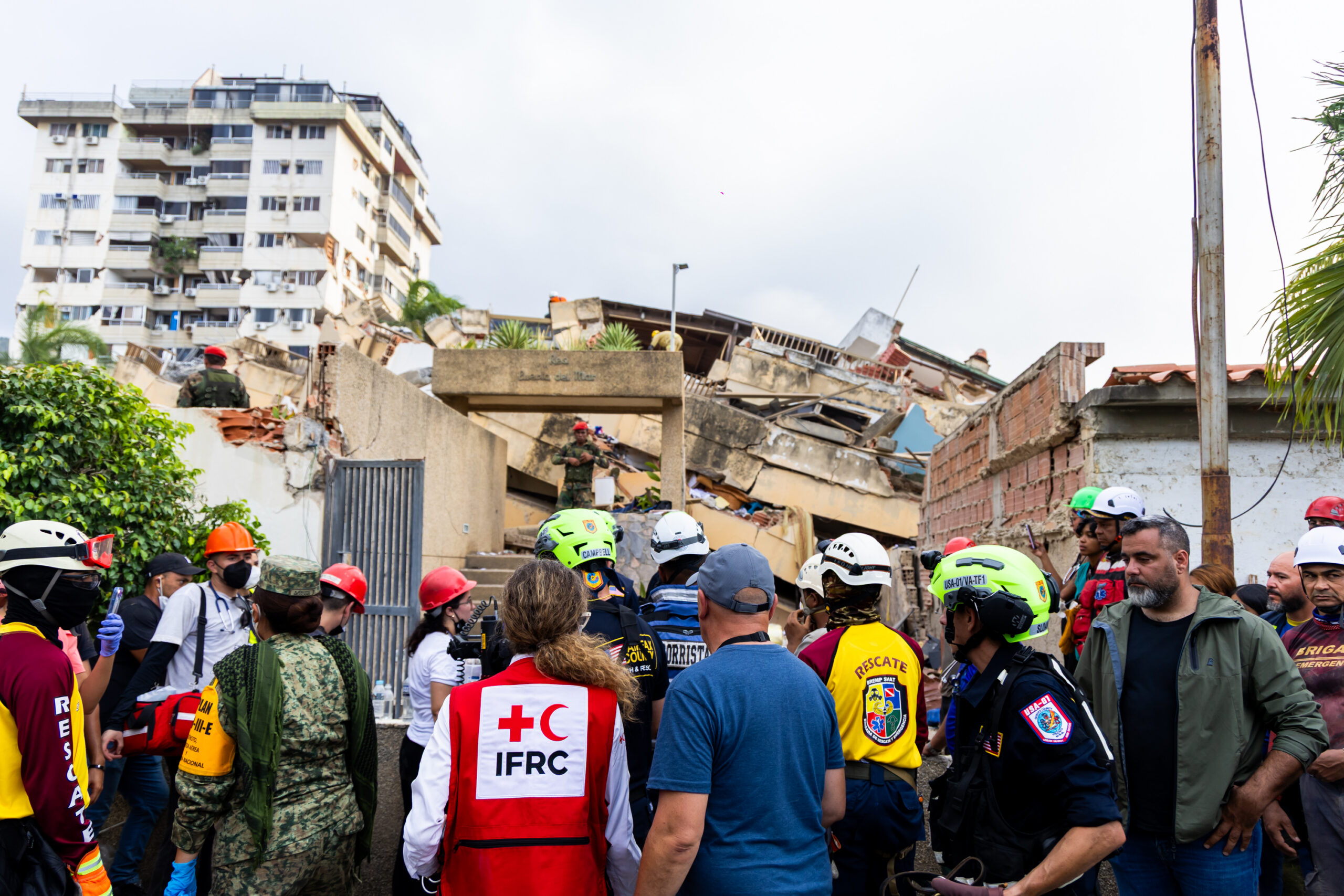 Emergency responders and Red Cross personnel assess a collapsed building following a disaster in an urban area